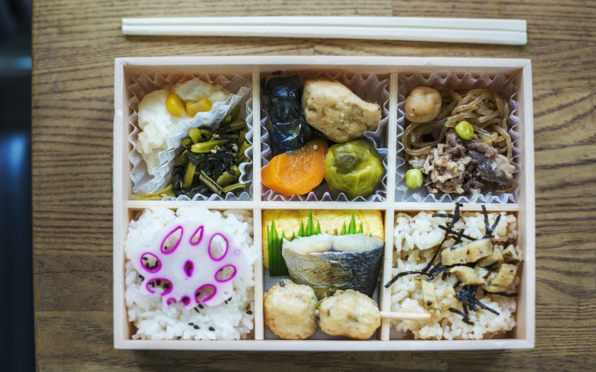 High angle close up of Bento box with traditional Japanese foods and chopsticks on a wooden table.