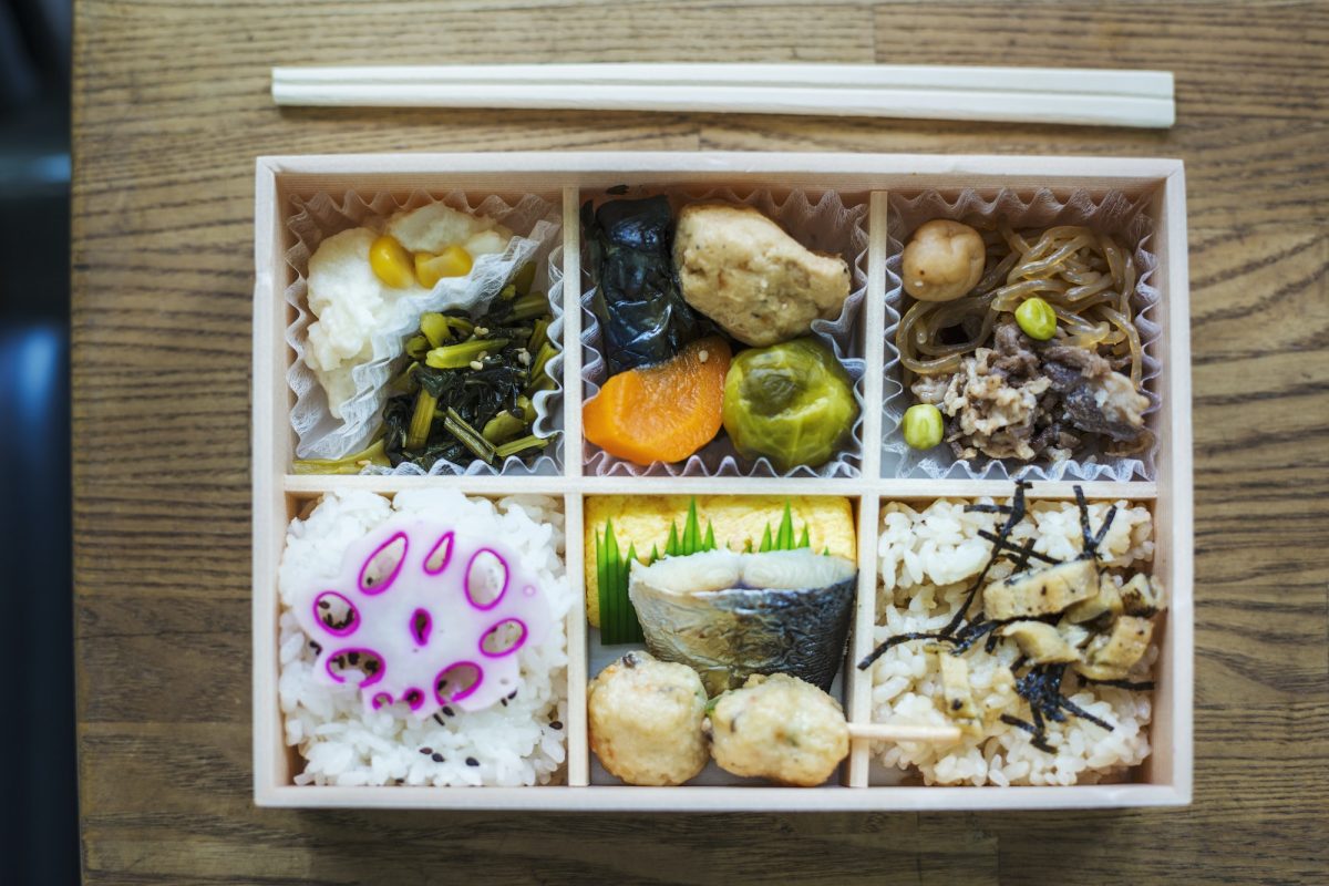 High angle close up of Bento box with traditional Japanese foods and chopsticks on a wooden table.