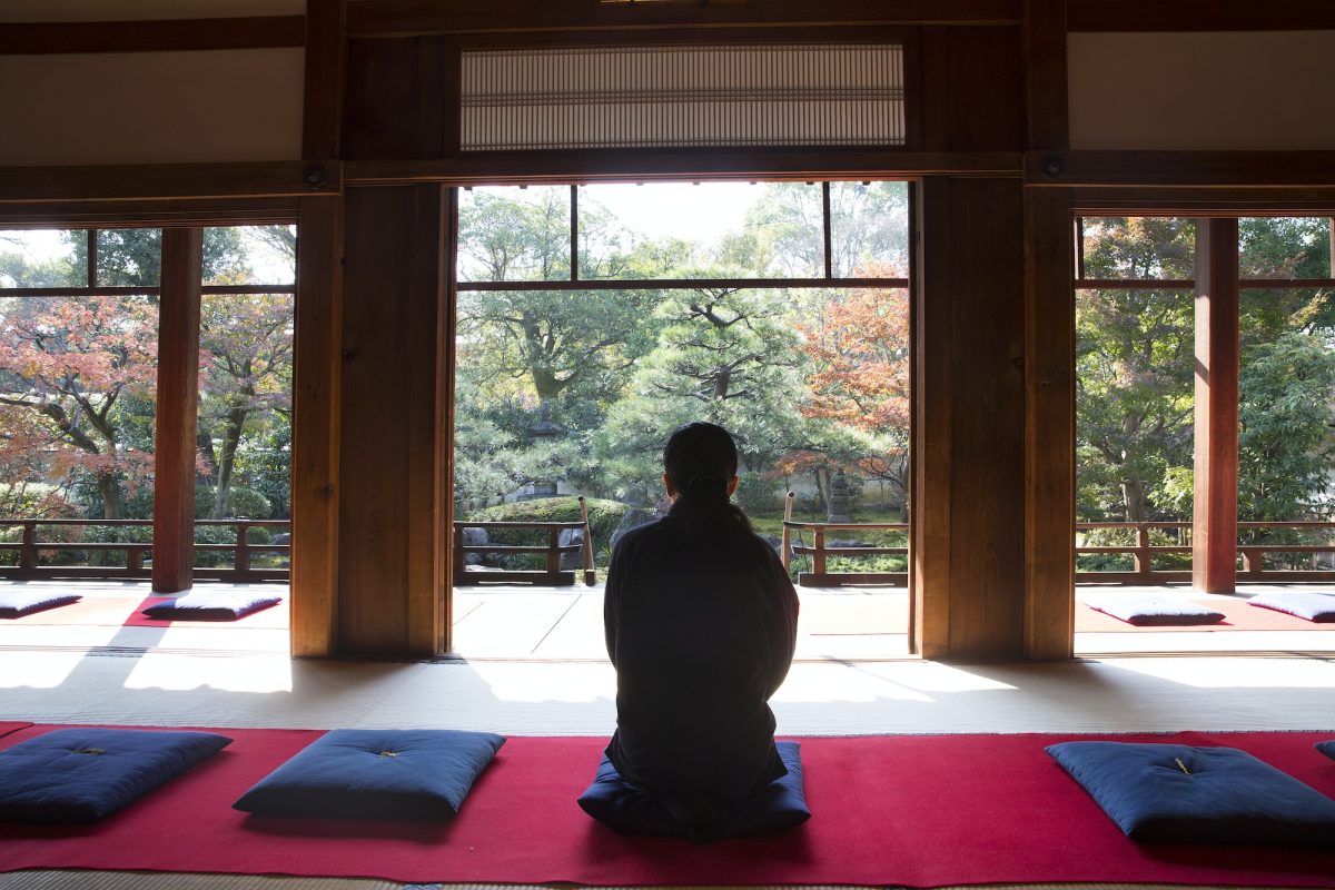 Rear view of man sitting on blue cushion on floor in traditional Japanese building.